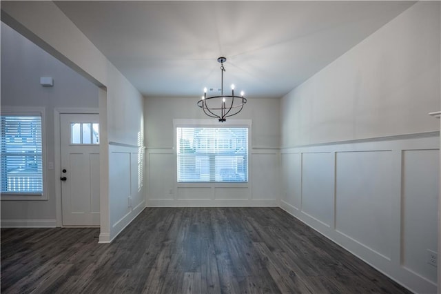 unfurnished dining area featuring a healthy amount of sunlight, dark wood-type flooring, and a chandelier