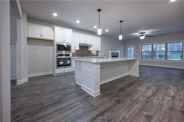 kitchen with a kitchen island with sink, hanging light fixtures, stainless steel appliances, light stone counters, and white cabinets