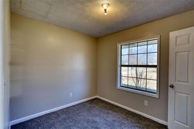 spare room featuring baseboards, dark colored carpet, and a textured ceiling