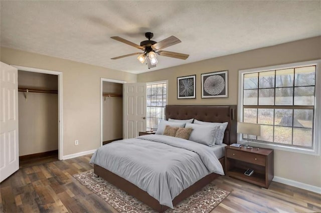 bedroom featuring a ceiling fan, wood finished floors, baseboards, and two closets