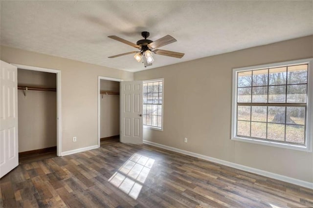 unfurnished bedroom featuring two closets, a ceiling fan, a textured ceiling, wood finished floors, and baseboards