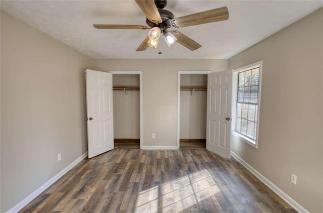 unfurnished bedroom with wood finished floors, two closets, and baseboards