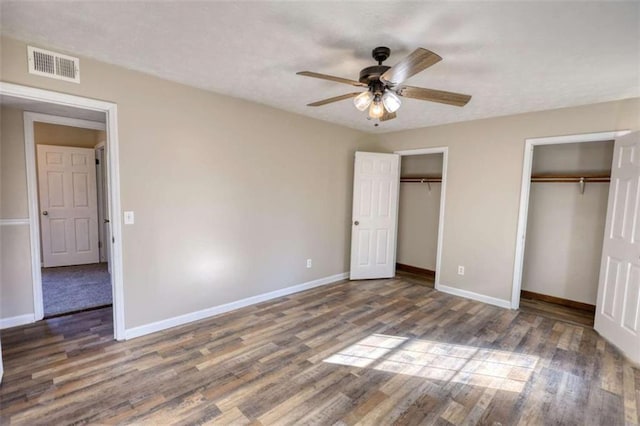 unfurnished bedroom featuring baseboards, wood finished floors, visible vents, and multiple closets