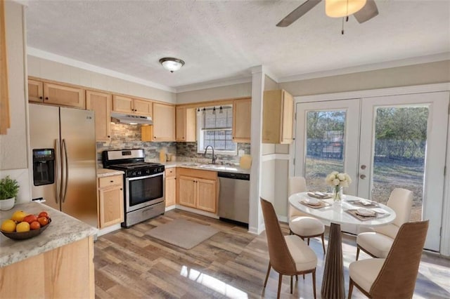 kitchen with light countertops, appliances with stainless steel finishes, light brown cabinets, a sink, and under cabinet range hood