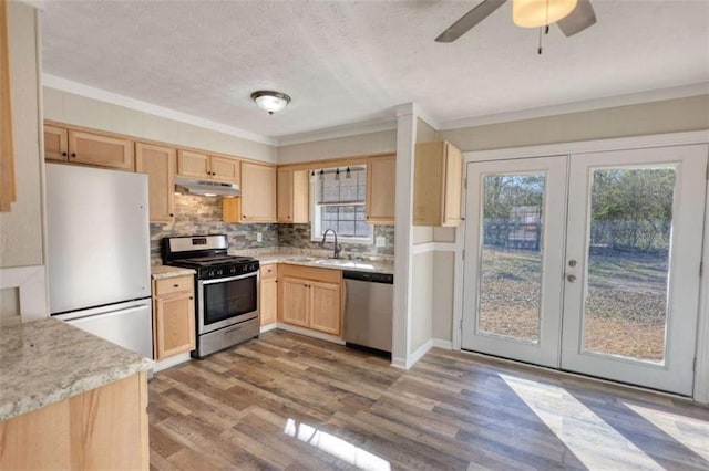 kitchen with light brown cabinets, under cabinet range hood, wood finished floors, appliances with stainless steel finishes, and tasteful backsplash