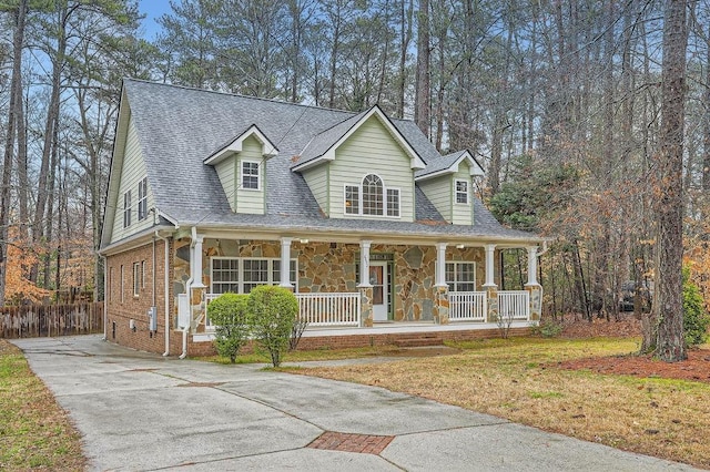 cape cod-style house with driveway, stone siding, a porch, roof with shingles, and brick siding