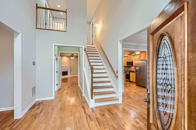 entrance foyer featuring visible vents, light wood-style flooring, stairway, baseboards, and a towering ceiling