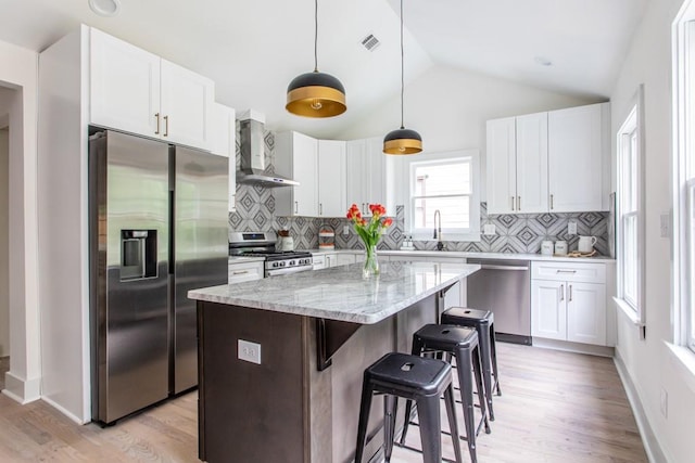 kitchen featuring lofted ceiling, appliances with stainless steel finishes, wall chimney exhaust hood, a kitchen island, and tasteful backsplash