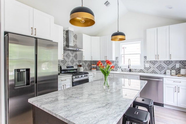 kitchen featuring lofted ceiling, backsplash, appliances with stainless steel finishes, and wall chimney range hood