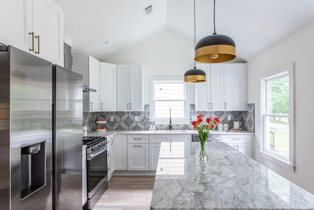 kitchen featuring decorative light fixtures, backsplash, stainless steel appliances, white cabinets, and vaulted ceiling