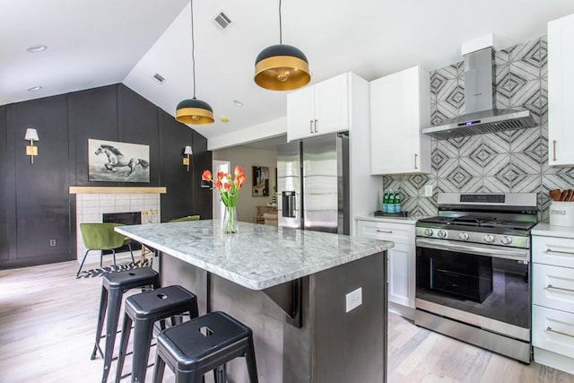 kitchen featuring appliances with stainless steel finishes, white cabinets, pendant lighting, wall chimney exhaust hood, and vaulted ceiling