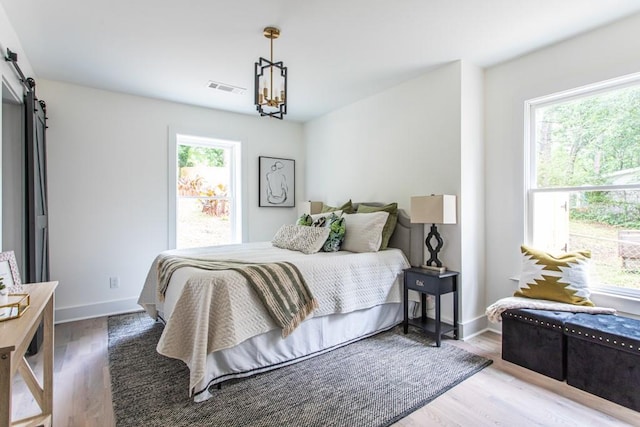 bedroom featuring a barn door, multiple windows, hardwood / wood-style flooring, and an inviting chandelier