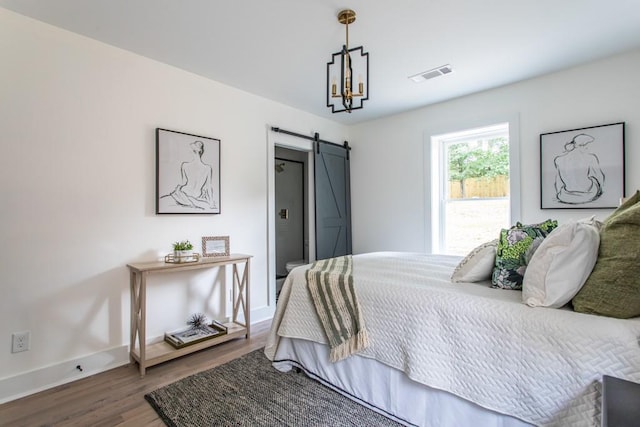 bedroom with a barn door, an inviting chandelier, and wood-type flooring