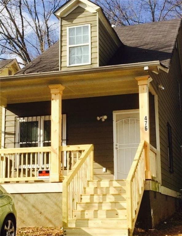 doorway to property featuring a porch and roof with shingles