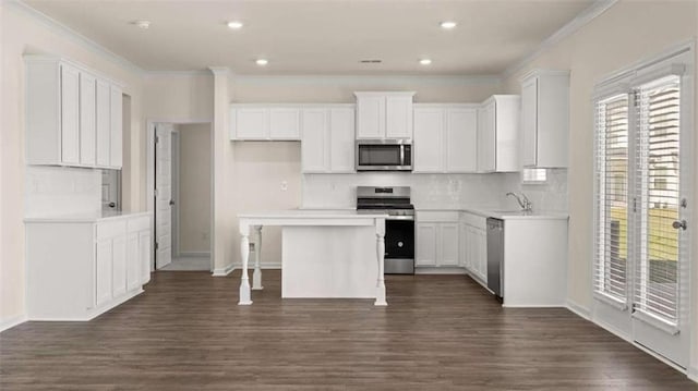 1139 Blue Juniper Cir, Loganville, GA 30052 - kitchen with crown molding, dark wood finished floors, white cabinetry, a kitchen island, and stainless steel appliances