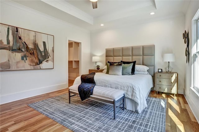 bedroom with wood-type flooring, ceiling fan, and a tray ceiling