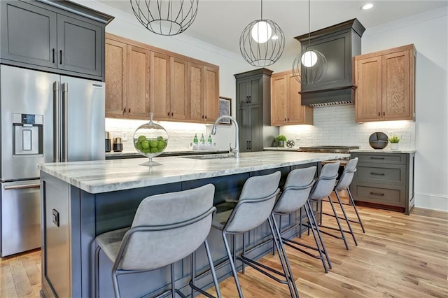 kitchen featuring decorative light fixtures, a center island with sink, high quality appliances, gray cabinets, and light stone countertops