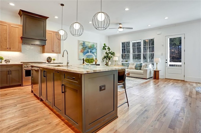 kitchen featuring an island with sink, sink, hanging light fixtures, light hardwood / wood-style floors, and light stone countertops