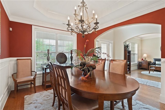 dining area featuring crown molding, arched walkways, wood finished floors, and a chandelier