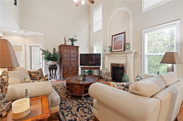 living area with wood finished floors, a high end fireplace, ceiling fan, visible vents, and a high ceiling