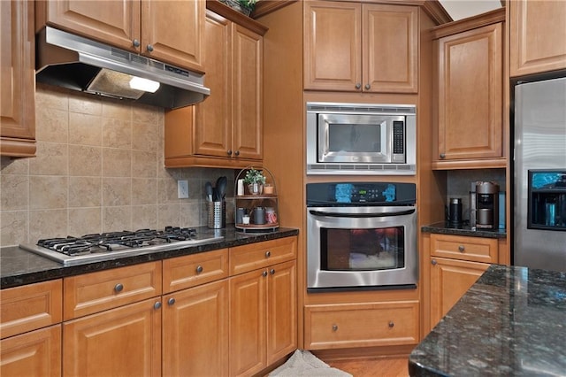 kitchen with dark stone counters, appliances with stainless steel finishes, under cabinet range hood, and tasteful backsplash