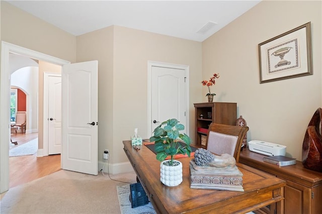 office with baseboards, arched walkways, and light colored carpet