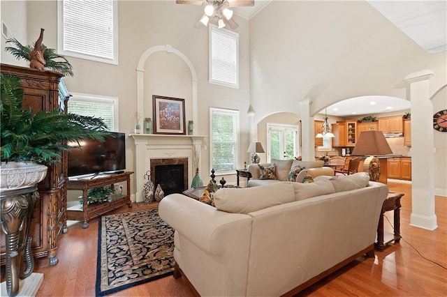 living area featuring arched walkways, a fireplace, light wood finished floors, a ceiling fan, and a towering ceiling