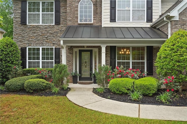 doorway to property featuring stone siding, a standing seam roof, metal roof, covered porch, and brick siding