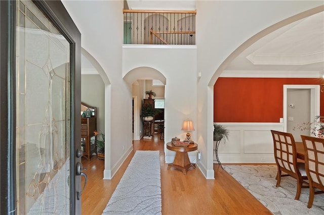 foyer featuring wood finished floors, arched walkways, crown molding, and a towering ceiling