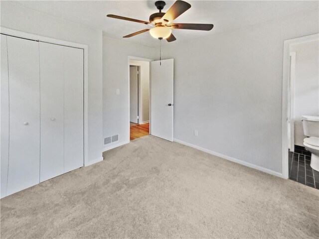 unfurnished bedroom featuring ensuite bath, ceiling fan, light colored carpet, and a closet