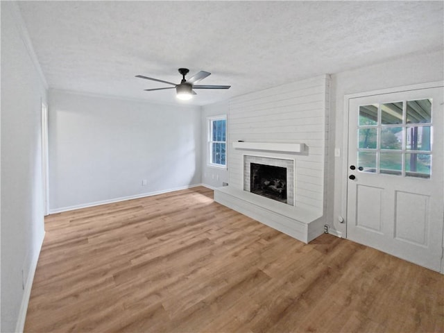 unfurnished living room with a textured ceiling, hardwood / wood-style flooring, ceiling fan, and a brick fireplace