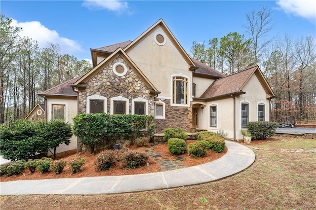 french country style house featuring stone siding, roof with shingles, and stucco siding