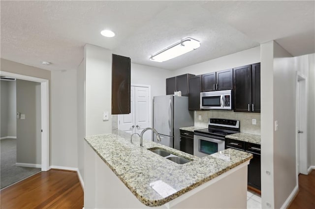 kitchen with a peninsula, a textured ceiling, appliances with stainless steel finishes, a sink, and backsplash