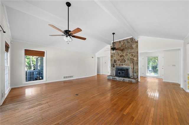 unfurnished living room featuring light hardwood / wood-style flooring, ceiling fan, lofted ceiling with beams, and a stone fireplace