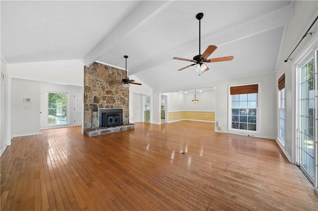 unfurnished living room with a fireplace, plenty of natural light, beamed ceiling, ceiling fan, and wood-type flooring