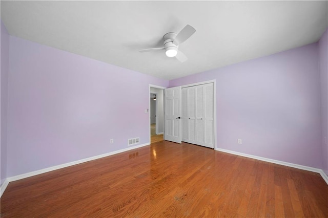 unfurnished bedroom with wood finished floors, baseboards, a closet, and visible vents
