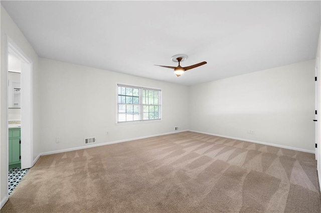 spare room with visible vents, light colored carpet, baseboards, and ceiling fan