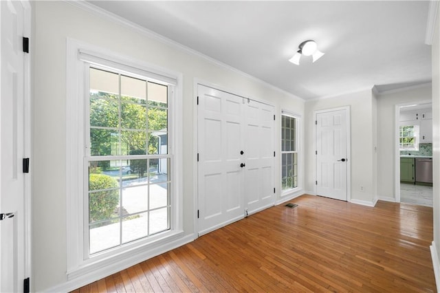 foyer with ornamental molding, wood-type flooring, baseboards, and visible vents