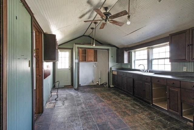 kitchen with dark countertops, vaulted ceiling, dark brown cabinets, and a sink