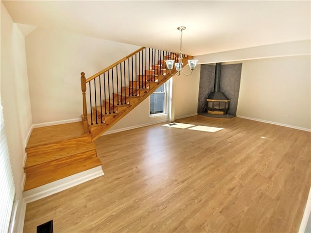 unfurnished living room featuring a notable chandelier, wood finished floors, visible vents, stairs, and a wood stove