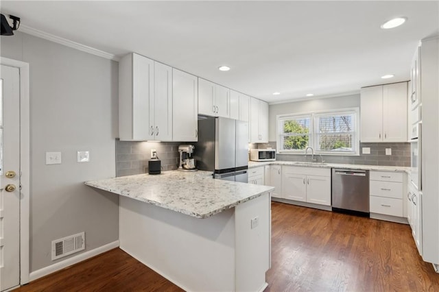 kitchen featuring a peninsula, a sink, visible vents, appliances with stainless steel finishes, and dark wood-style floors