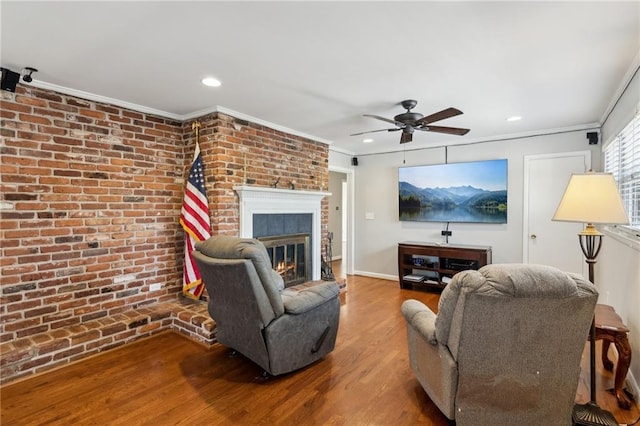 living room featuring a brick fireplace, crown molding, brick wall, and wood finished floors