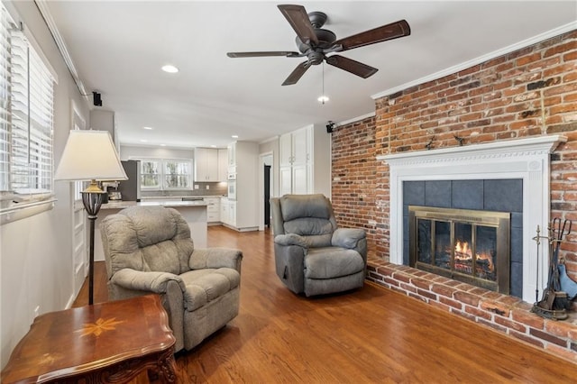 living room with crown molding, a fireplace, light wood finished floors, recessed lighting, and a ceiling fan