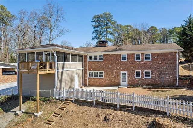 rear view of house featuring a fenced front yard, a sunroom, brick siding, and a chimney