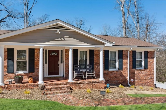 view of front of house featuring a porch, a shingled roof, and brick siding