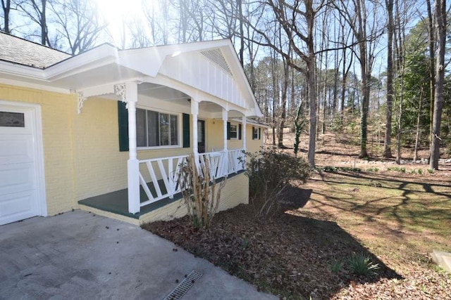 view of side of property with brick siding, covered porch, a shingled roof, and a garage