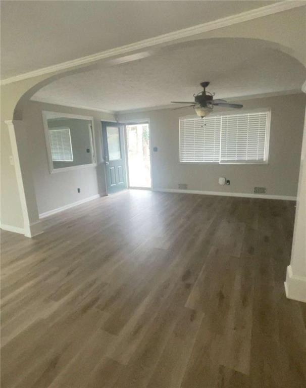 unfurnished living room with wood finished floors, arched walkways, and ornamental molding