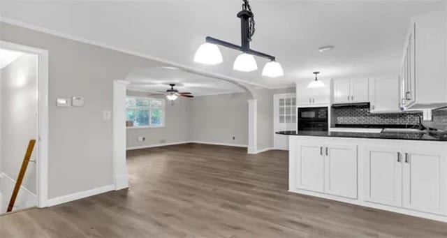 kitchen featuring dark countertops, tasteful backsplash, arched walkways, white cabinets, and black microwave