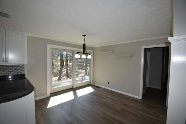 unfurnished dining area featuring a notable chandelier, dark wood-type flooring, baseboards, and ornamental molding