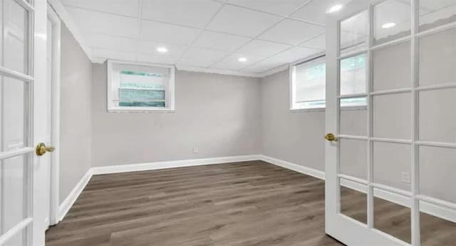 below grade area with a wealth of natural light, a paneled ceiling, baseboards, and wood finished floors